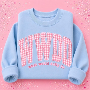 May include: A light blue crewneck sweatshirt featuring the large pink and white gingham patterned letters WWDD arched across the chest, with the text what would dolly do printed in smaller pink letters directly underneath the large letters.