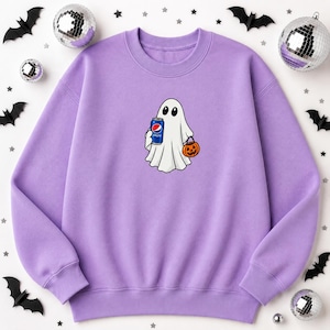 May include: A light purple crewneck sweatshirt featuring a central graphic of a white ghost holding a blue soda can with the Pepsi logo and an orange jack-o'-lantern pumpkin bucket. The design is centered on the chest of the long-sleeved garment.