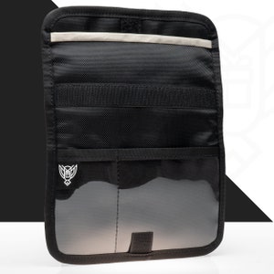 Può includere: Organizzatore per auto nero con più tasche e una sezione trasparente. L'organizzatore ha una forma rettangolare e presenta un logo bianco nell'angolo in basso a sinistra. Una striscia di colore chiaro è in alto.