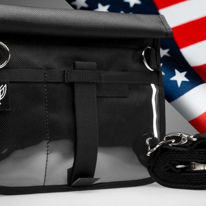 May include: Black tactical utility pouch with a clear front pocket, a zippered closure, and an adjustable strap. The pouch has a logo with a stylized eagle design.