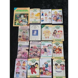 Könnte beinhalten: Eine Sammlung von Vintage-Schnittmustern für Cabbage Patch Kids-Puppen. Die Muster stammen von Butterick und Simplicity und zeigen verschiedene Puppenoutfits. Das Bild enthält ein Buch mit dem Titel "Designer Clothes from The Cabbage Patch."
