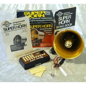 Könnte beinhalten: Ein Cal Custom Super Horn elektronisch programmierbares Musikhorn-Set, bestehend aus einem goldfarbenen Horn, einem Steuergerät mit Holzoptik-Paneel und weißen Tasten, einer Installationsanleitung, einem Liederbuch, einem Karton und kleinem Montagematerial.