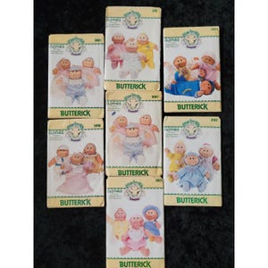 Könnte beinhalten: Eine Sammlung von Butterick-Schnittmustern für Cabbage Patch Kids-Kleidung. Die Muster zeigen Illustrationen der Puppen in verschiedenen Outfits, mit dem Butterick-Logo und den Musternummern auf den Umschlägen. Die Muster sind in verschiedenen Farben.