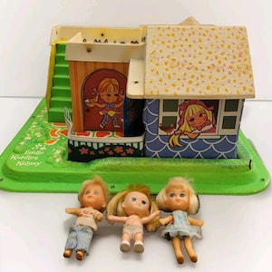 May include: Vintage Little Kiddles Kolony playset with three small dolls. The playset features a two-story house with a green base, a yellow roof, and illustrations of children. The dolls have blonde hair and are wearing various outfits.