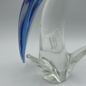 K&ouml;nnte beinhalten: Eine klare Glasskulptur mit blau-silbernem Akzent. Die Skulptur hat eine geschwungene, organische Form mit einem Etikett mit der Aufschrift "formia vetri di murano made in italy".