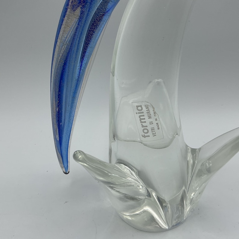 K&ouml;nnte beinhalten: Eine klare Glasskulptur mit blau-silbernem Akzent. Die Skulptur hat eine geschwungene, organische Form mit einem Etikett mit der Aufschrift "formia vetri di murano made in italy".