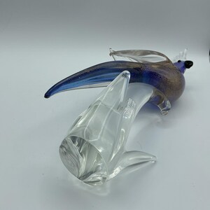 K&ouml;nnte beinhalten: Eine Glasskulptur eines Vogels mit blauen und goldenen Akzenten, die auf einem klaren Glassockel sitzt. Der Vogel hat einen langen, gebogenen Schnabel und ausgebreitete Fl&uuml;gel. Auf dem Sockel steht das Wort "Formia".