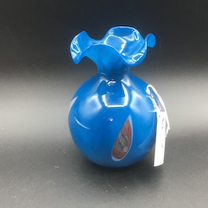 May include: A bright blue glass vase with a ruffled rim. The vase has a rounded body with white and red accents. This decorative vase is ideal for displaying flowers or as a standalone art piece.