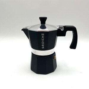 Peut inclure: Une cafetière italienne noire et argentée avec une base octogonale et une poignée noire. Le mot GROSCHE est imprimé verticalement en blanc sur la partie supérieure noire. Elle possède un couvercle argenté avec un bouton noir et une petite valve.