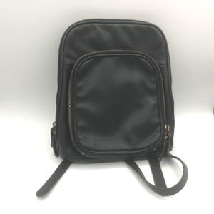 May include: Black leather backpack with a zippered main compartment and a smaller zippered front pocket. The backpack has adjustable shoulder straps and a top handle. The zippers are a brass colour. The bag is made of a smooth, matte leather.