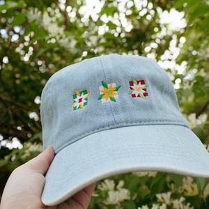 May include: A light blue denim baseball cap with three embroidered flower designs in yellow, red, and green.