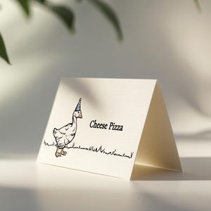 Op de afbeelding: Een gevouwen kaart met een grillige illustratie van een gans met een feesthoed, staand op een graslijn. De tekst "Cheese Pizza" staat rechts van de gans gedrukt. De kaart is gebroken wit en geplaatst tegen een zachte, neutrale achtergrond.