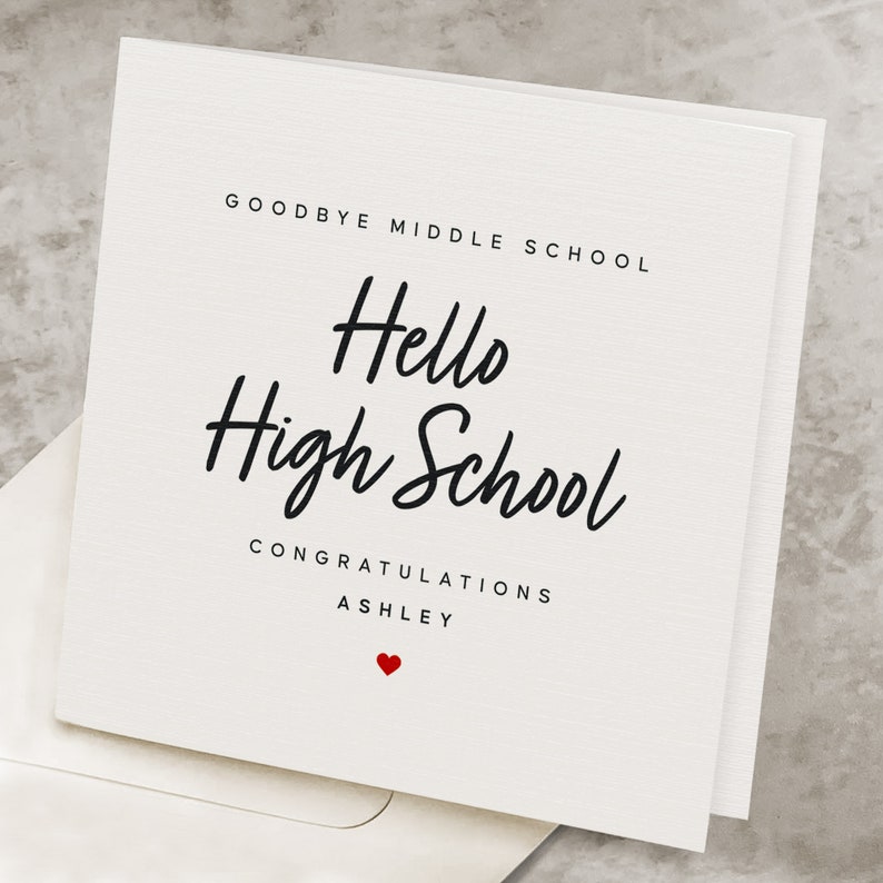 May include: White card with black text that reads "Goodbye Middle School Hello High School Congratulations Ashley" with a red heart symbol.