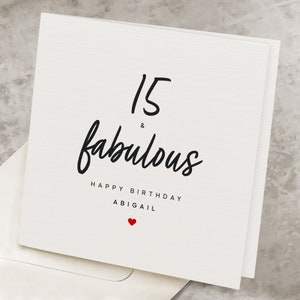May include: White card with black text that reads "15 & fabulous Happy Birthday Abigail" with a small red heart at the bottom.