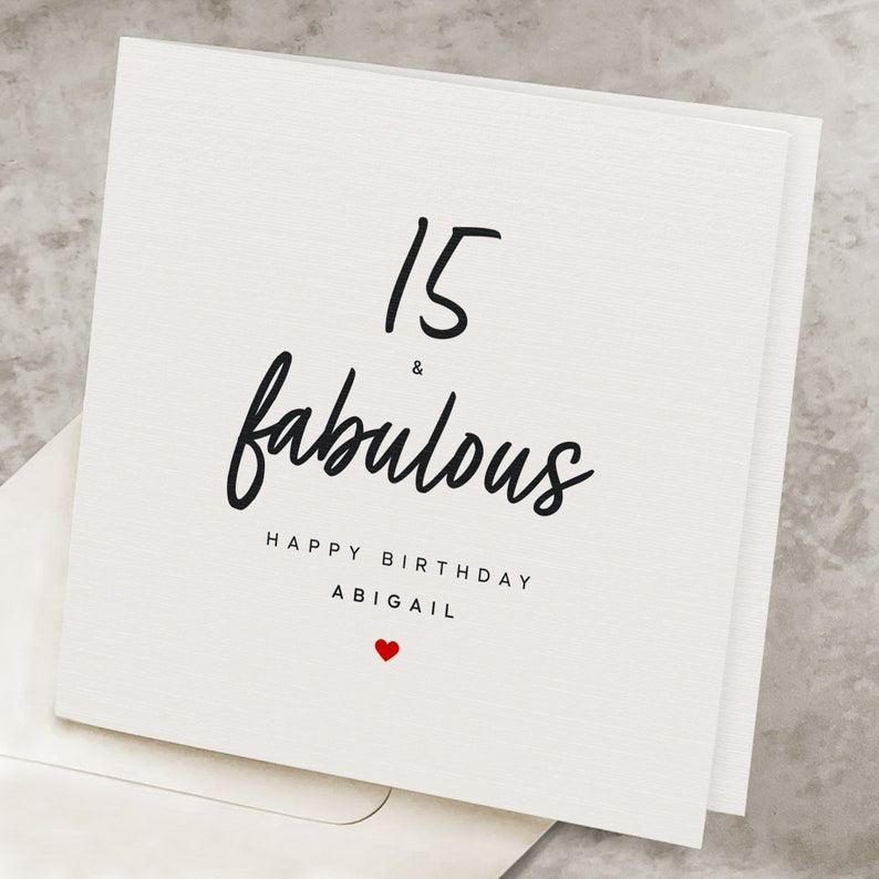 May include: White card with black text that reads "15 & fabulous Happy Birthday Abigail" with a small red heart at the bottom.