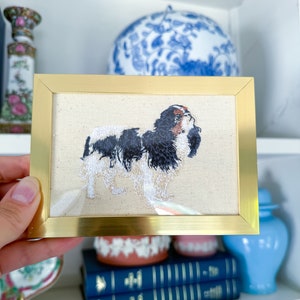 May include: An embroidered picture of a Cavalier King Charles Spaniel dog, framed in gold.