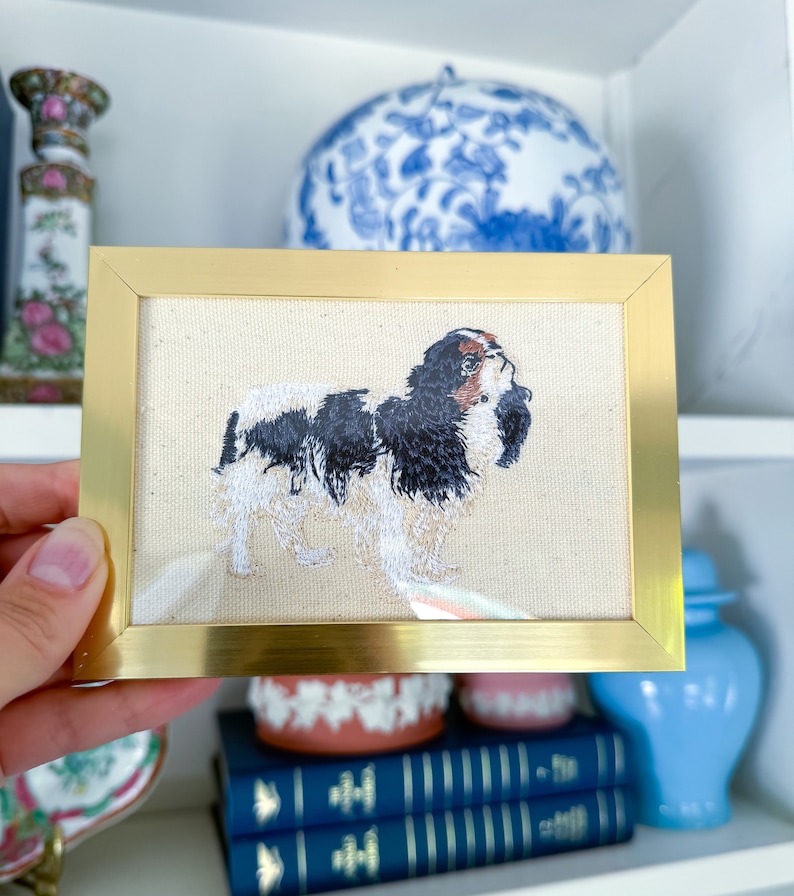 May include: An embroidered picture of a Cavalier King Charles Spaniel dog, framed in gold.