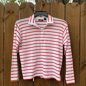 May include: White long-sleeve shirt with red horizontal stripes and a single button closure at the collar. The shirt has a green label with the text "Talbots" on it.