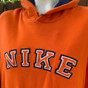 Peut inclure: Sweat &agrave; capuche orange avec le mot "NIKE" en lettres blanches bord&eacute;es de bleu marine. Le sweat &agrave; capuche a une doublure int&eacute;rieure bleu marine dans la capuche. Le sweat &agrave; capuche est fait d'une mati&egrave;re douce et confortable.