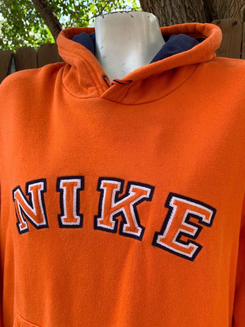Peut inclure: Sweat &agrave; capuche orange avec le mot "NIKE" en lettres blanches bord&eacute;es de bleu marine. Le sweat &agrave; capuche a une doublure int&eacute;rieure bleu marine dans la capuche. Le sweat &agrave; capuche est fait d'une mati&egrave;re douce et confortable.