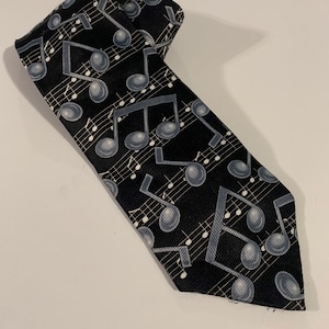 May include: A black silk tie with a repeating pattern of silver musical notes and treble clefs.