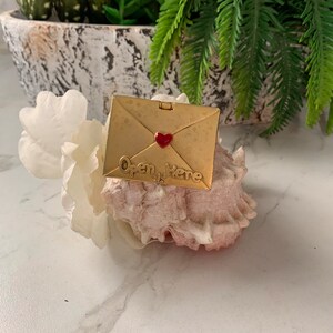 May include: Gold-colored envelope charm with a red heart and the words "Open Here" on a seashell.