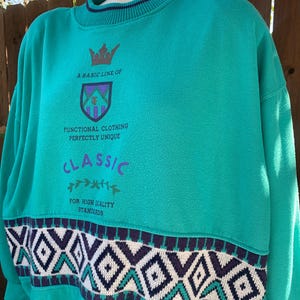 Puede incluir: Sudadera de color turquesa con un estampado geom&eacute;trico en blanco, turquesa y morado. El texto en la sudadera dice "A BASIC LINE OF FUNCTIONAL CLOTHING PERFECTLY UNIQUE CLASSIC FOR HIGH QUALITY STANDARDS". El cuello es turquesa con una raya azul marino.