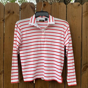 May include: White long-sleeve shirt with red horizontal stripes and a single button closure at the collar. The shirt has a green label with the text "Talbots" on it.
