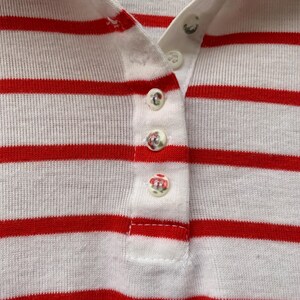 May include: Close-up of a white and red striped shirt with a button-up collar. The shirt has five white buttons down the front.