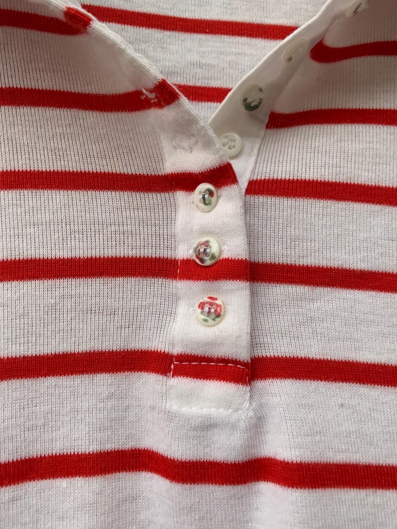May include: Close-up of a white and red striped shirt with a button-up collar. The shirt has five white buttons down the front.