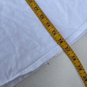 Pu&ograve; includere: Un tessuto bianco con un metro a nastro giallo posizionato sopra. Il nastro mostra misure da 45,7 cm a 76,2 cm. Il tessuto sembra essere a trama semplice, con una cucitura visibile.