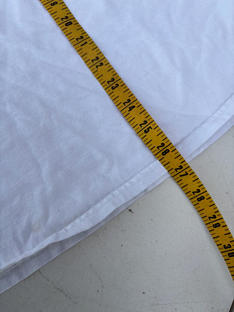 Pu&ograve; includere: Un tessuto bianco con un metro a nastro giallo posizionato sopra. Il nastro mostra misure da 45,7 cm a 76,2 cm. Il tessuto sembra essere a trama semplice, con una cucitura visibile.