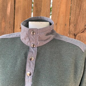 May include: A green and gray long-sleeved shirt with a button-up collar and a textured fabric.