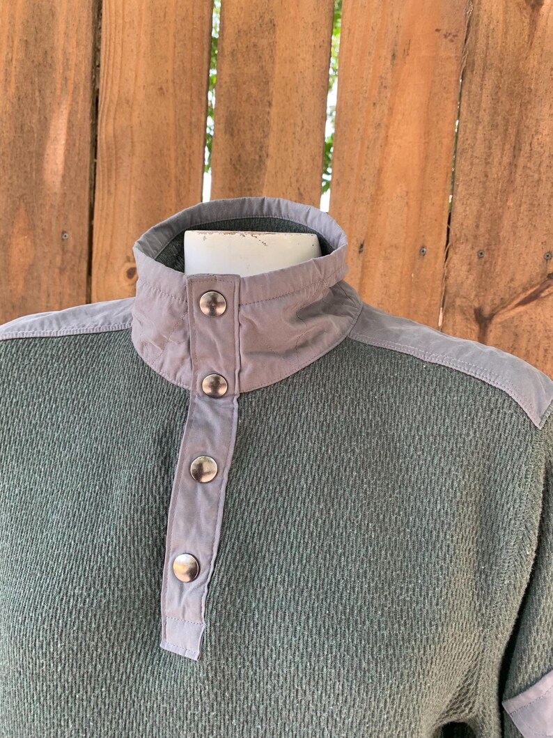 May include: A green and gray long-sleeved shirt with a button-up collar and a textured fabric.
