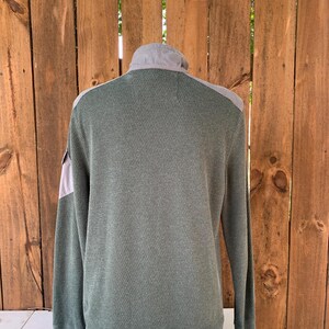 May include: A long-sleeved, green waffle-knit shirt with a gray panel on the shoulders and a zippered collar.