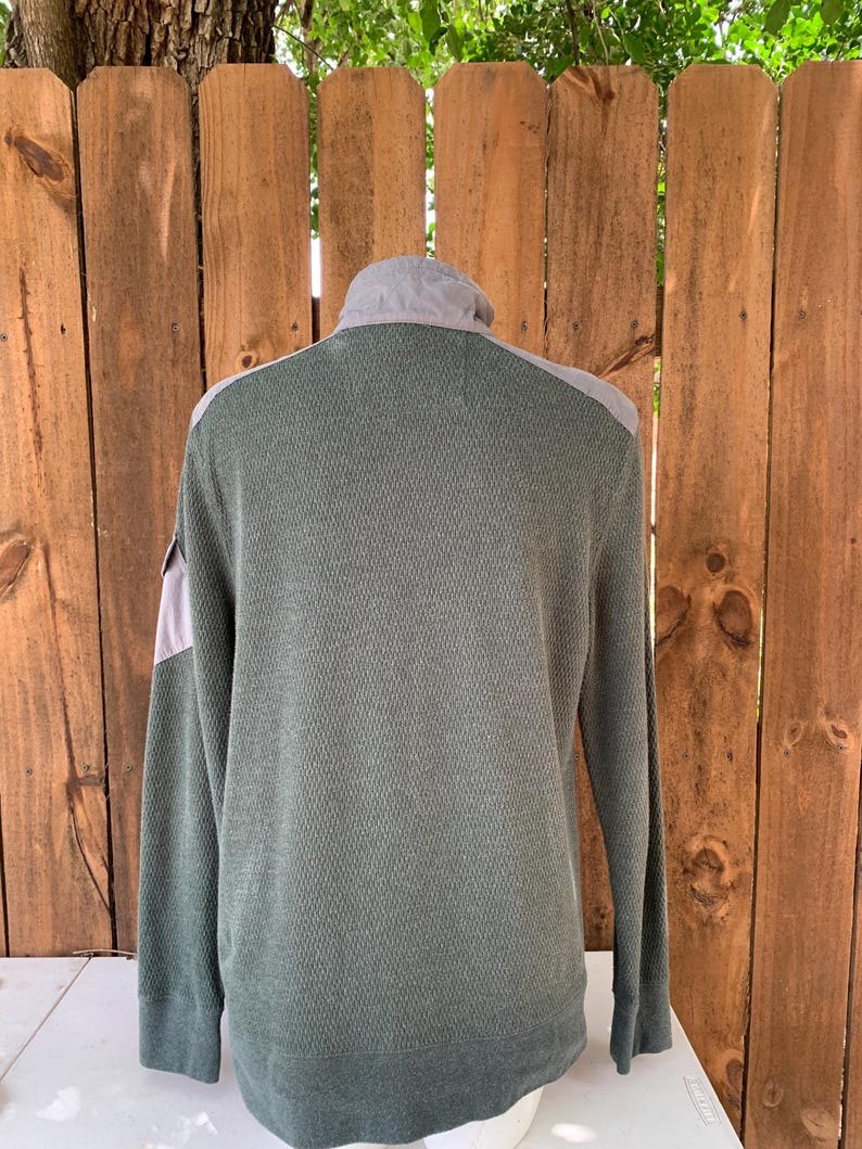 May include: A long-sleeved, green waffle-knit shirt with a gray panel on the shoulders and a zippered collar.