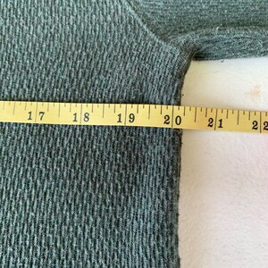 May include: Close-up of a dark green fabric with a textured pattern. A measuring tape is placed along the edge of the fabric, showing measurements from 17 to 22 inches.