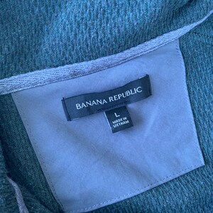 May include: A dark green, textured, long-sleeved shirt with a black label that reads "Banana Republic" and "L" for size. The label also says "Made in Vietnam".
