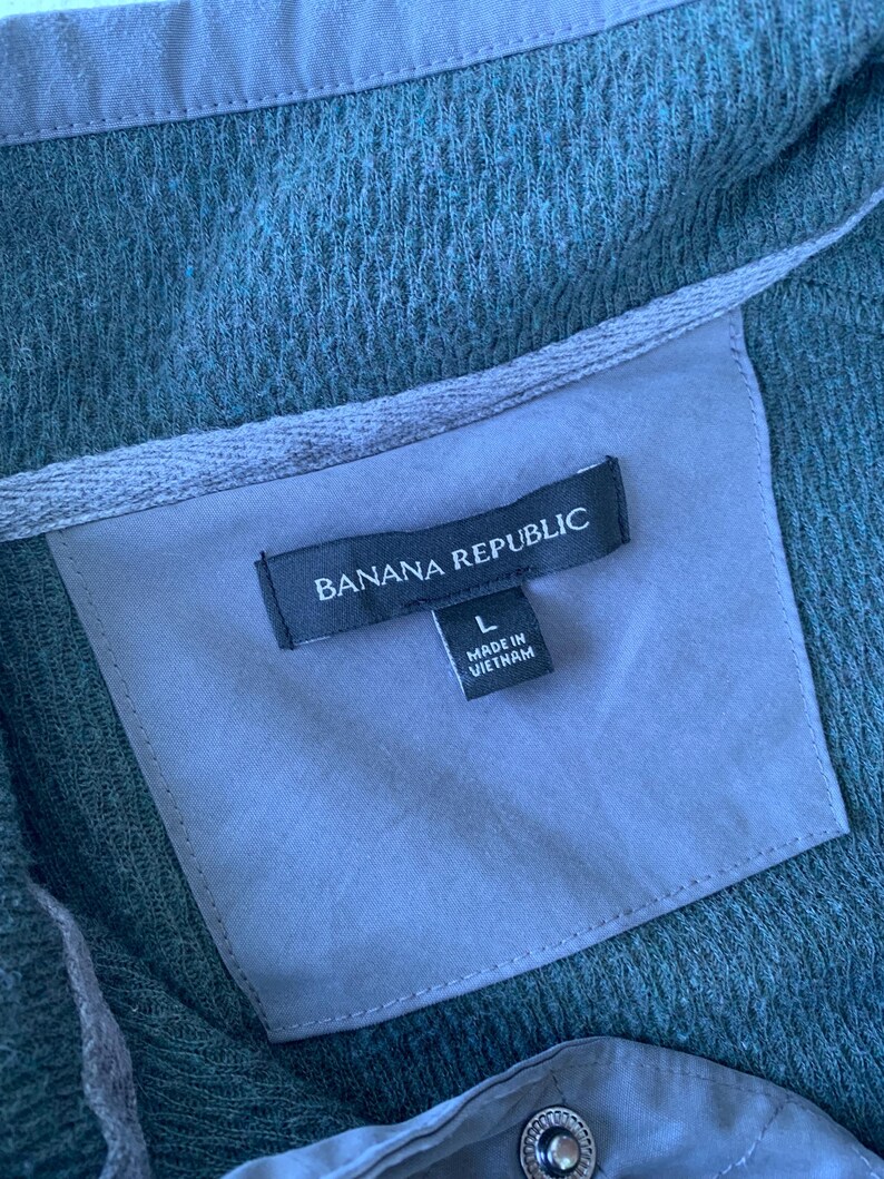 May include: A dark green, textured, long-sleeved shirt with a black label that reads "Banana Republic" and "L" for size. The label also says "Made in Vietnam".