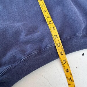 May include: A navy blue sweatshirt with a yellow measuring tape laid across it. The tape shows measurements from 14 to 29 inches. The sweatshirt's hem is visible at the bottom of the frame.