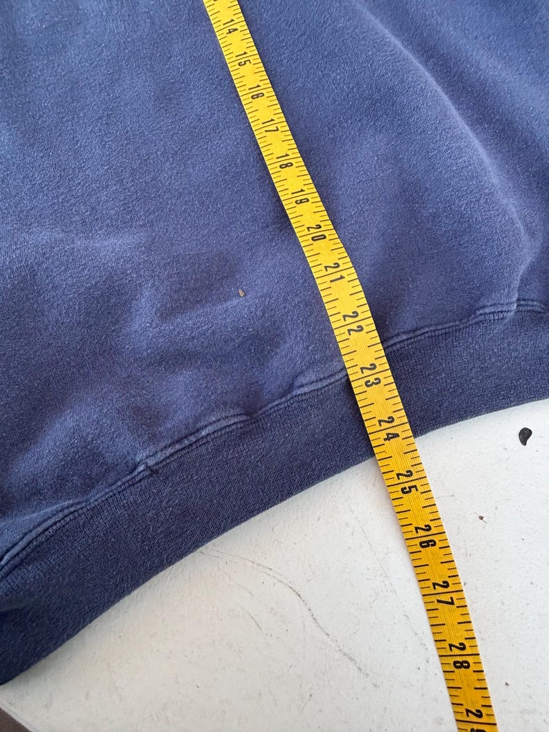 May include: A navy blue sweatshirt with a yellow measuring tape laid across it. The tape shows measurements from 14 to 29 inches. The sweatshirt's hem is visible at the bottom of the frame.