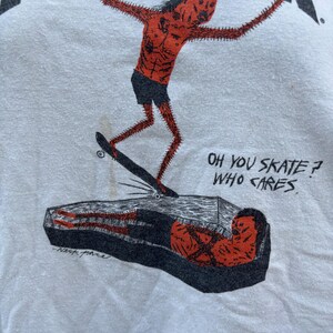 Pu&ograve; includere: T-shirt bianca con una grafica di una figura rossa e appuntita che fa skateboard su una bara. La parola "THRASHER" &egrave; stampata in alto. Il testo sulla maglietta recita "OH YOU SKATE? WHO CARES."