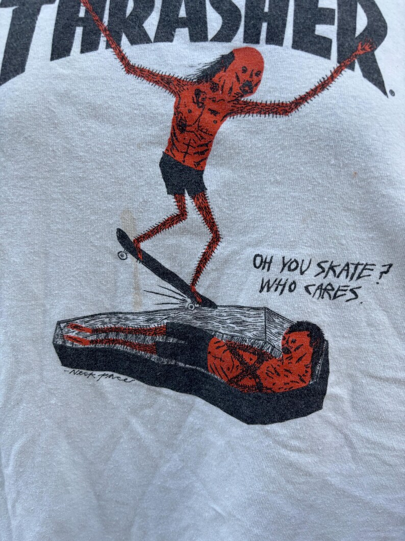 Pu&ograve; includere: T-shirt bianca con una grafica di una figura rossa e appuntita che fa skateboard su una bara. La parola "THRASHER" &egrave; stampata in alto. Il testo sulla maglietta recita "OH YOU SKATE? WHO CARES."
