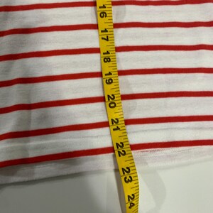 May include: A white and red striped fabric with a yellow measuring tape. The tape measures 25 inches.