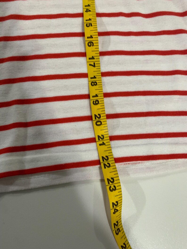 May include: A white and red striped fabric with a yellow measuring tape. The tape measures 25 inches.