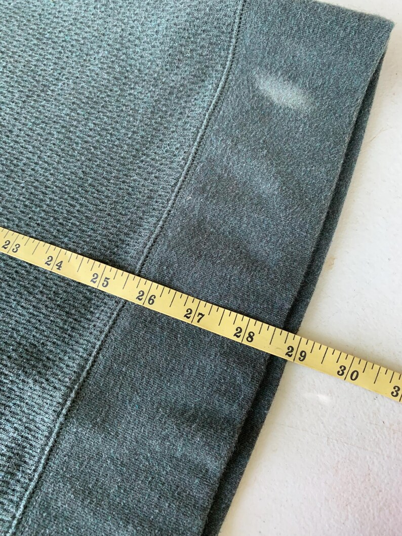 May include: Close-up of a dark green fabric with a measuring tape showing 23 to 31 inches.