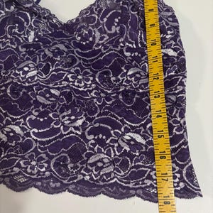 May include: A purple lace camisole with silver floral detailing. The camisole has thin straps and a scalloped hem. The length of the camisole is approximately 18 inches.