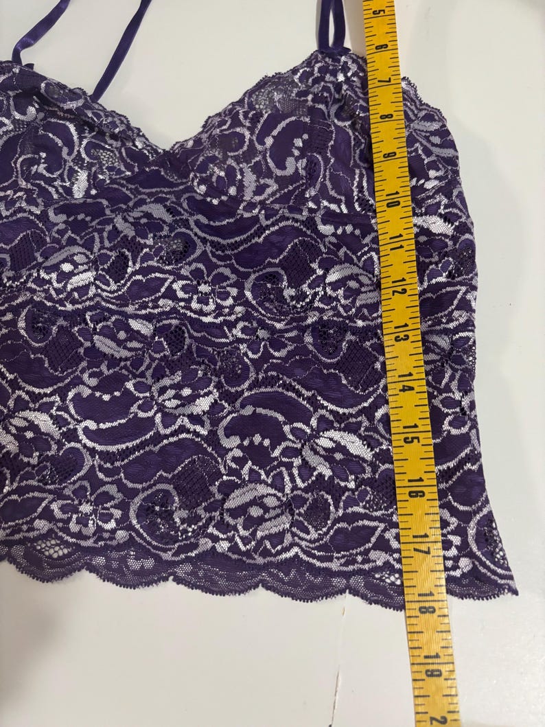 May include: A purple lace camisole with silver floral detailing. The camisole has thin straps and a scalloped hem. The length of the camisole is approximately 18 inches.