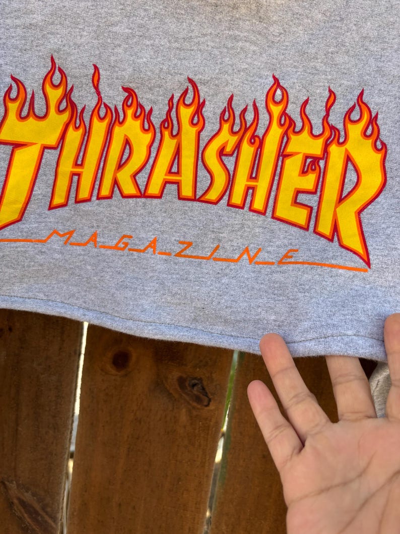 May include: Gray t-shirt featuring the Thrasher Magazine logo in yellow and orange flames. The word "Magazine" is printed in orange below the main logo. The shirt is made of a soft, comfortable material.