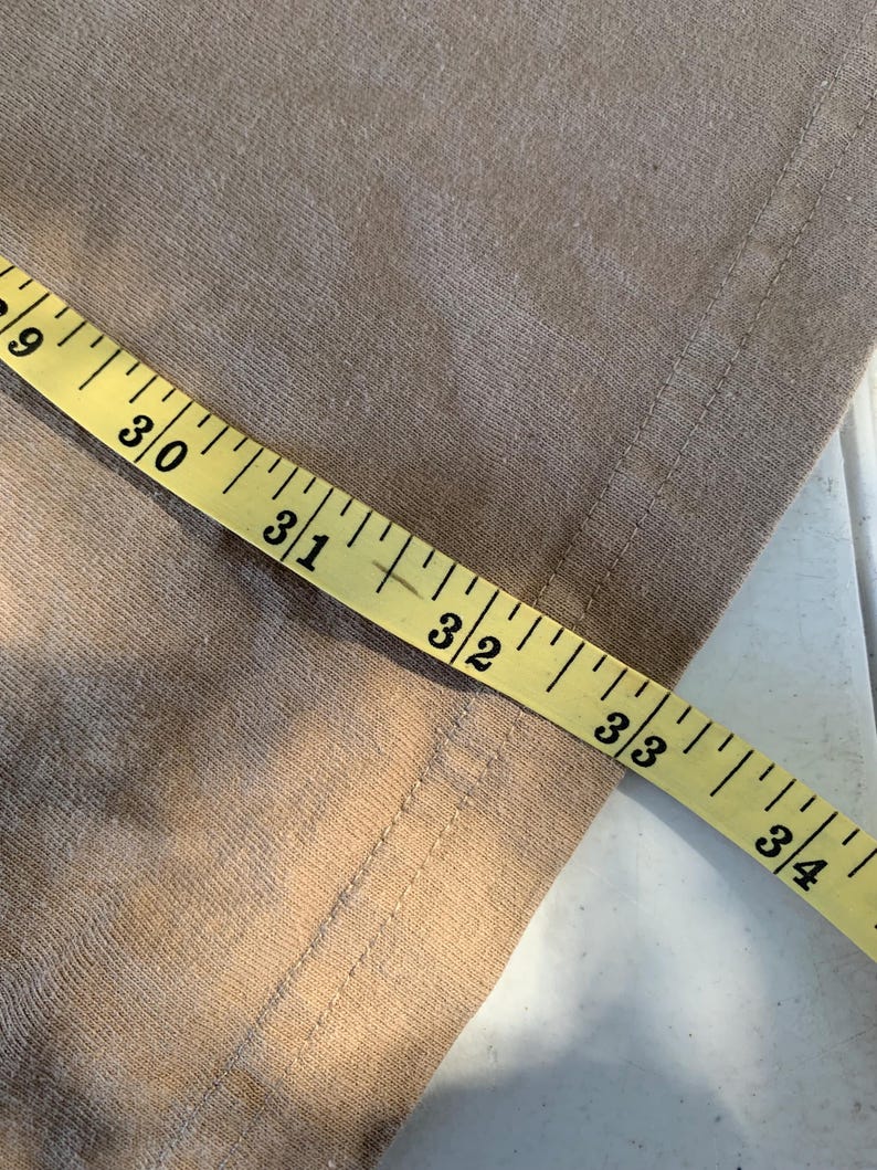 K&ouml;nnte beinhalten: Nahaufnahme eines beigefarbenen Stoffes mit einem gelben Ma&szlig;band. Das Band zeigt Messungen von 73,66 cm bis 86,36 cm. Der Stoff hat eine sichtbare Naht am Rand.
